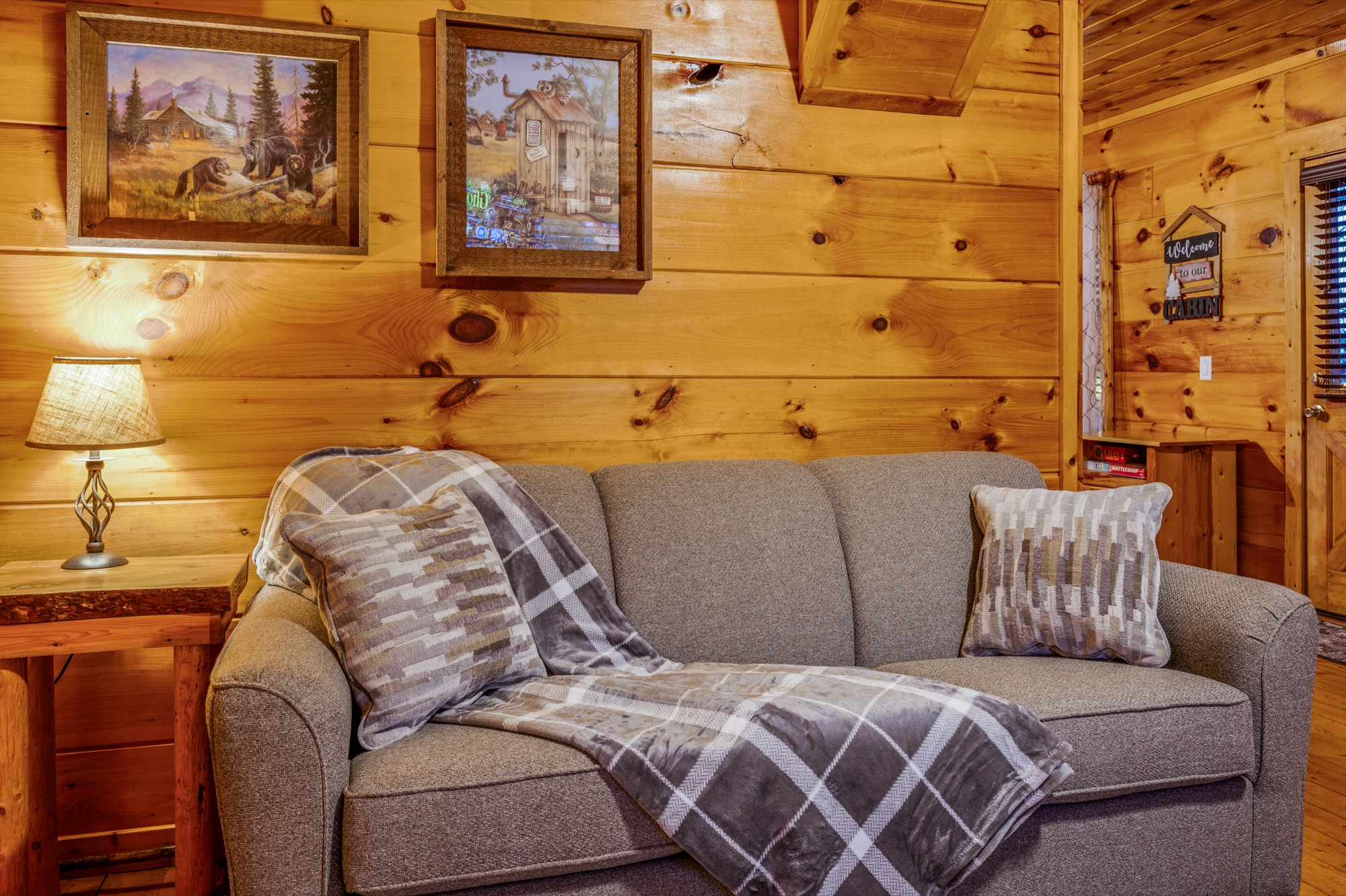 Sitting nook off Bearadise's bunk room with a gray sofa, framed woodland prints, and a Welcome to Our Cabin sign